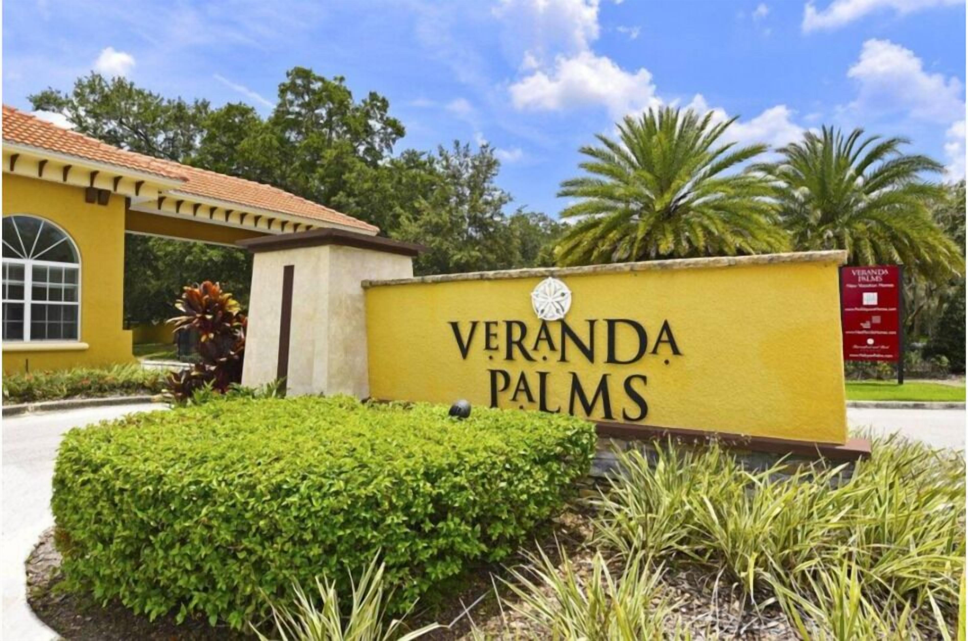 Un letrero amarillo con la inscripción 'VERANDA PALMS', rodeado de follaje y palmeras.