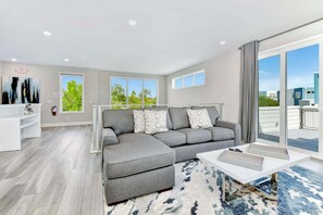 A modern living room with a grey sectional sofa, a white coffee table, and a large window offering a view of greenery and buildings. - Private Condo, Ideal for Groups. Duplex - 236 (Kissimmee)