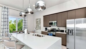 Een moderne keuken met een centraal eiland, roestvrijstalen apparatuur en hangende lampen.