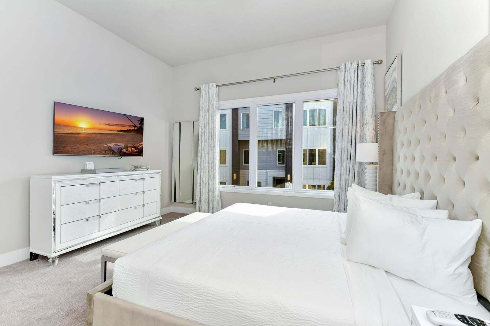 A bedroom with a large bed, a dresser, a television, and a window with curtains.