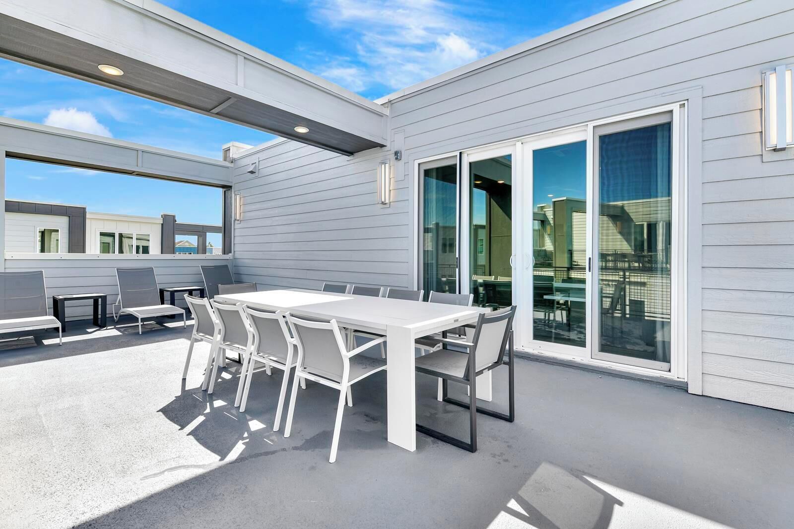 An outdoor patio with a white table and chairs, large sliding glass doors, and a view of the surrounding buildings.