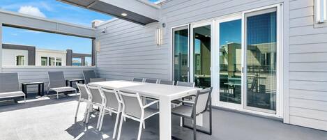 An outdoor patio with a white table and chairs, large sliding glass doors, and a view of the surrounding buildings.