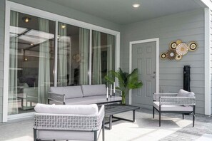 A covered patio area with a sofa, two chairs, a coffee table, and a door. - Modern 5-bedroom Home With Private Pool and Resort Access! (Davenport)