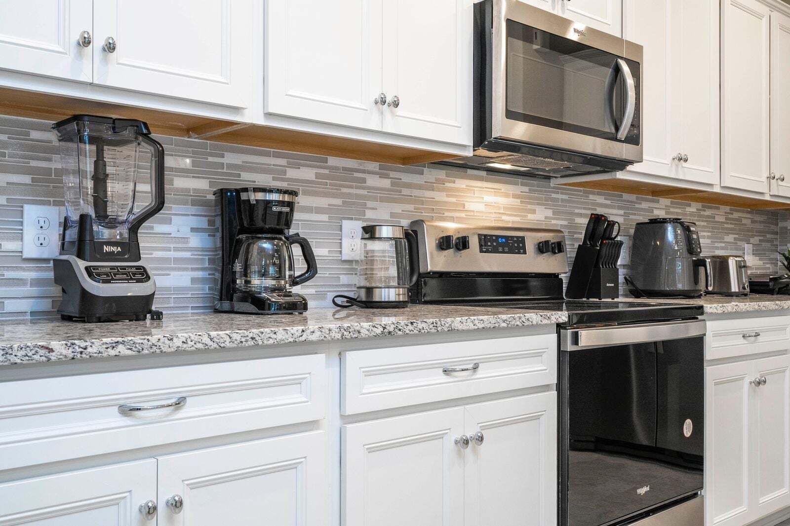 Una cocina con gabinetes blancos, microondas, cafetera, licuadora y tostadora.