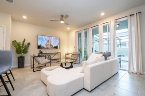 A modern living room with a sofa, armchairs, a coffee table, a TV, and a ceiling fan. - Modern 5-bedroom Home With Private Pool and Resort Access! (Davenport)