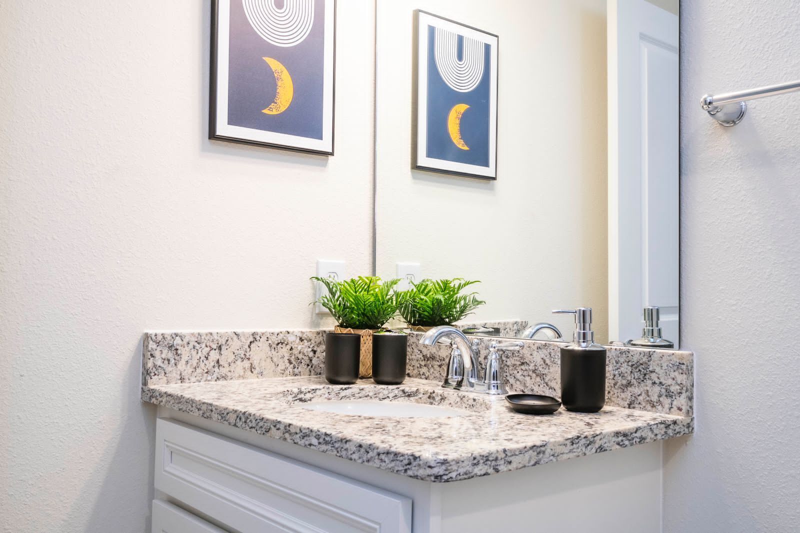 Een badkamer met een granieten blad, een wastafel, een spiegel en twee ingekaderde decoratieve wandobjecten.