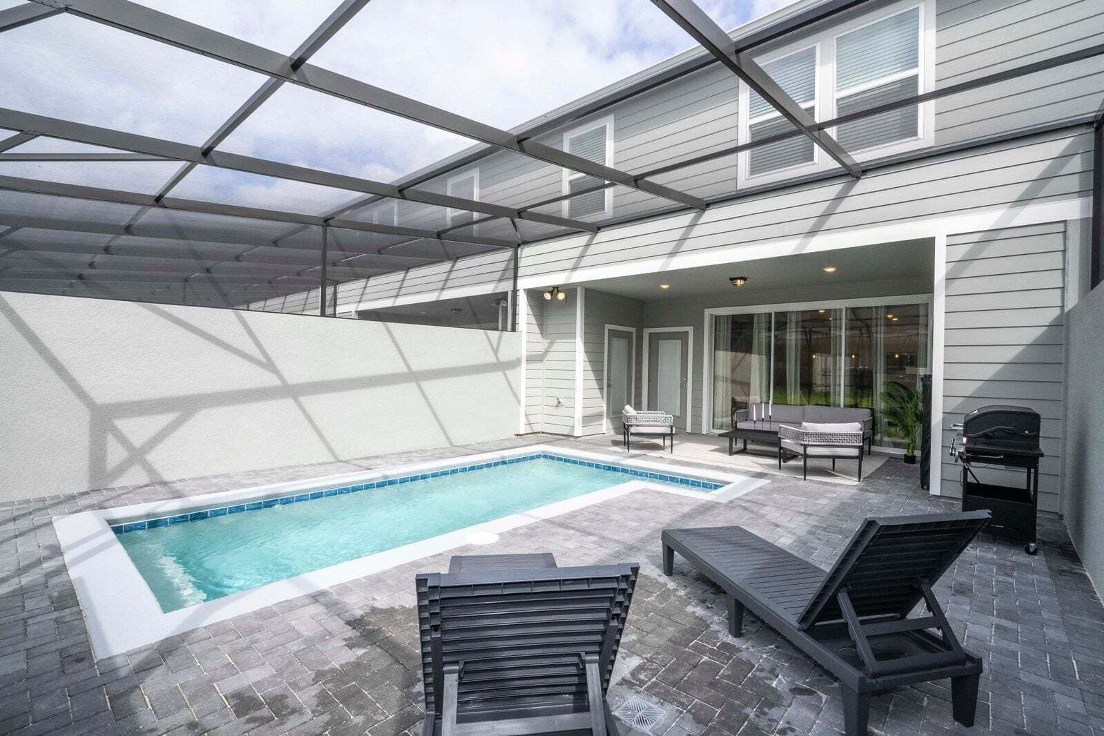 A covered outdoor swimming pool with lounge chairs and a grill area.