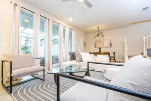 A modern living room with a glass coffee table, a sofa, and a chair. - Modern 5-bedroom Home With Private Pool and Resort Access! (Davenport)