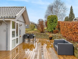 Eine Holzterrasse mit Gartenmöbeln, einem kleinen Schuppen und einer Hecke.