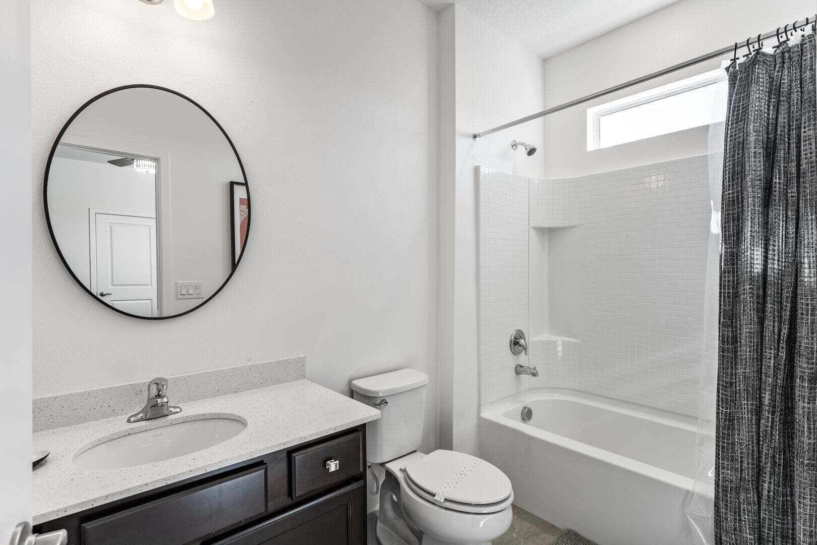 Ein modernes Badezimmer mit einem runden Spiegel, einem Waschbecken, einer Toilette und einer Badewanne.