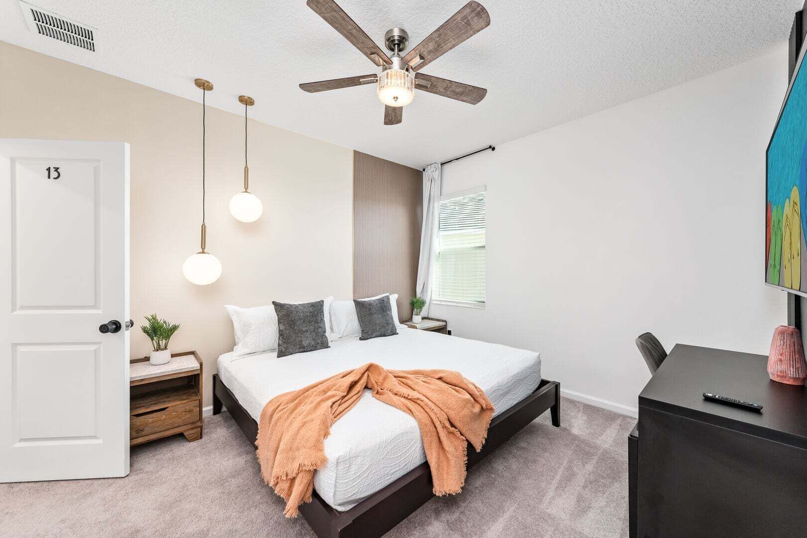 A bedroom with a bed, bedside table, nightstand, ceiling fan, and a window with blinds.