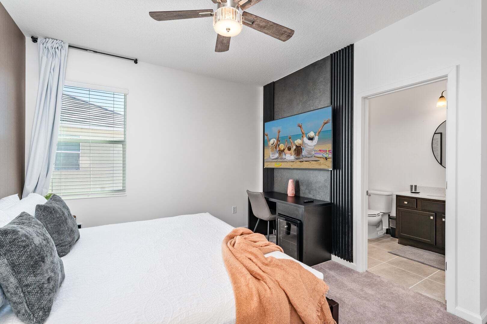 A bedroom with a bed, a desk, a television, and a bathroom visible through an open door.