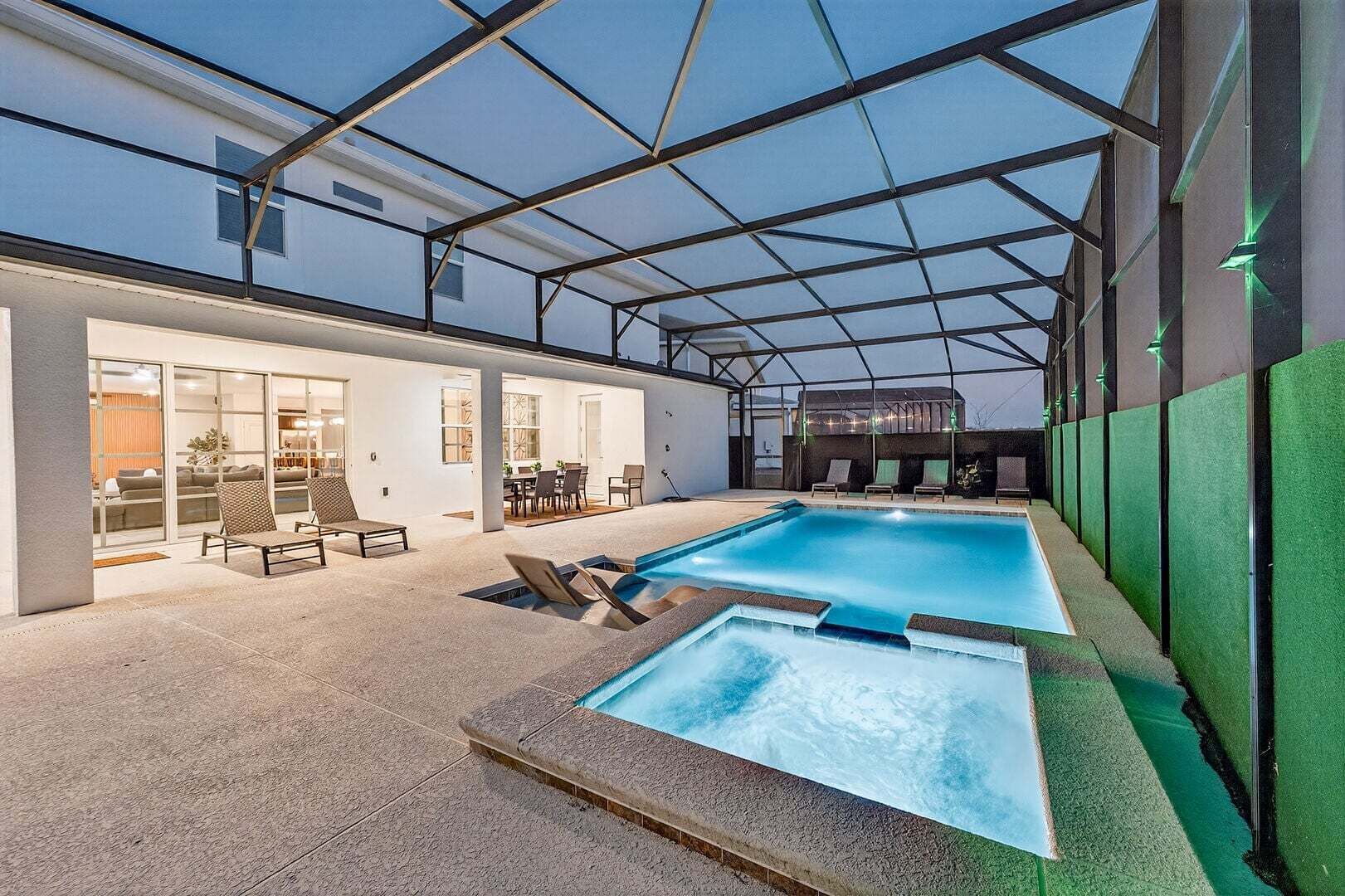 Una piscina con cerramiento de vidrio, sillas de descanso y una zona de terraza.
