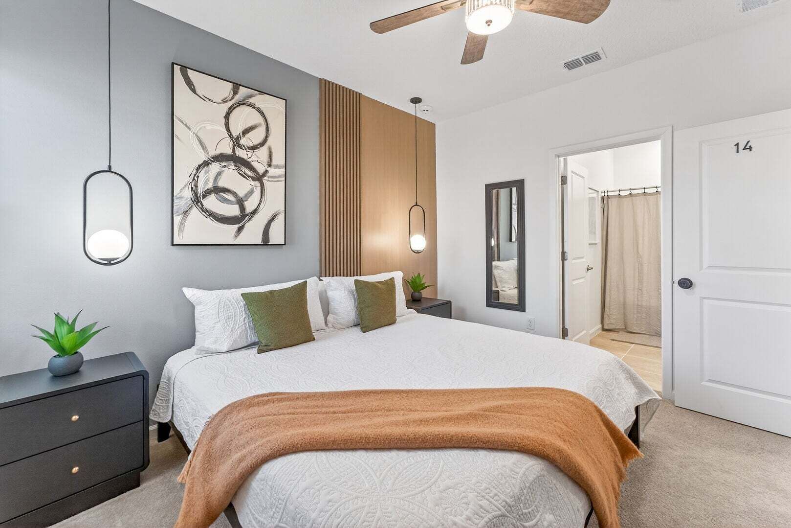 A modern bedroom with a bed, bedside tables, a mirror, and a ceiling fan.