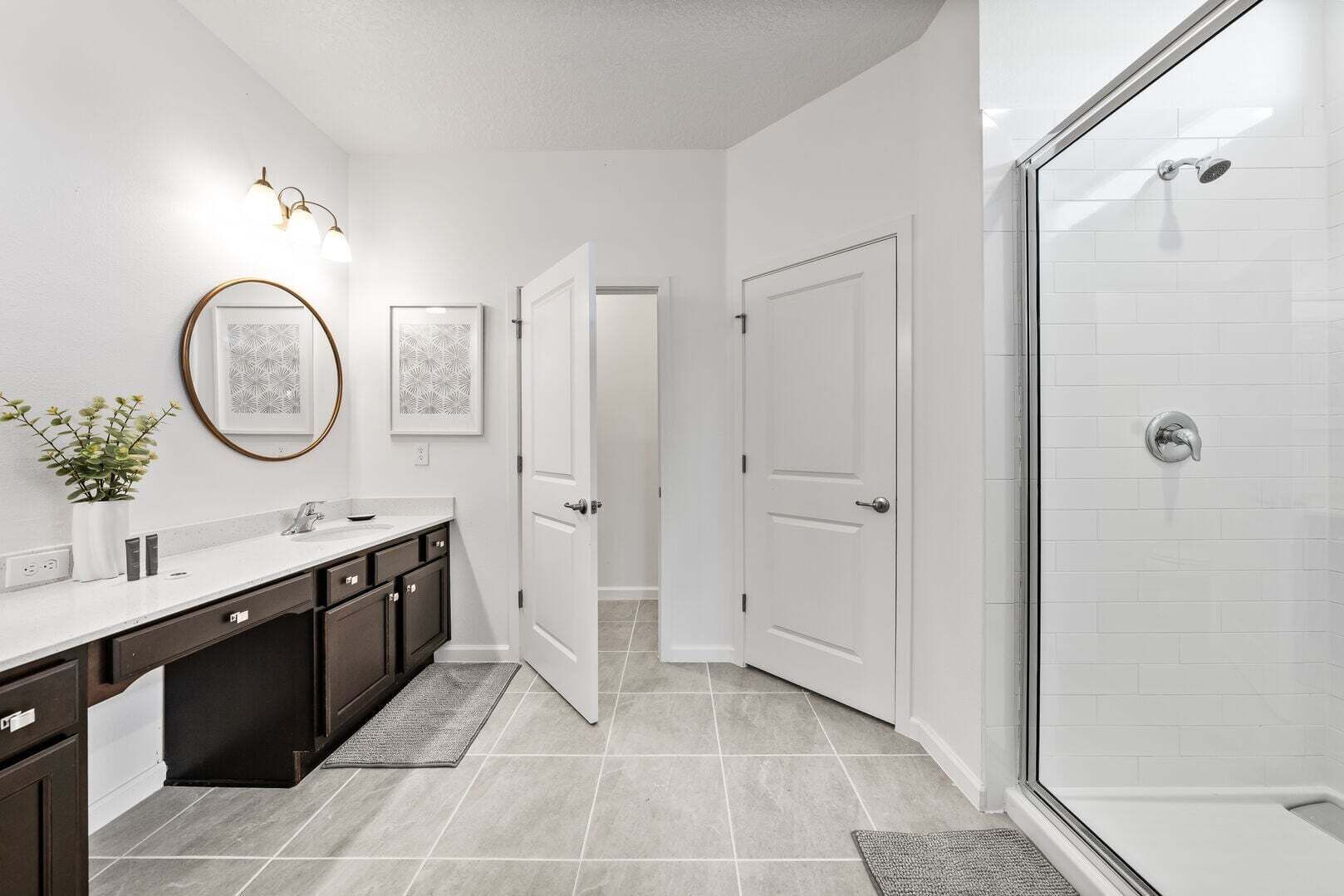 A modern bathroom with a shower, a sink with dark cabinets, and a white tiled floor.