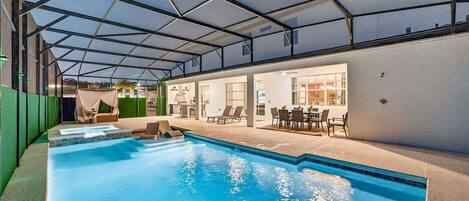 An indoor swimming pool with a covered area, lounge chairs, and a dining setup.