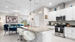 Una cocina moderna con armarios blancos, encimera de granito, electrodomésticos de acero inoxidable y una zona de comedor con sillas azules.