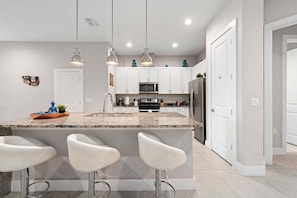 A modern kitchen with a granite countertop, stainless steel appliances, and pendant lighting. - Townhouse 4 Bedrooms 5 Min to Disney! (Kissimmee)