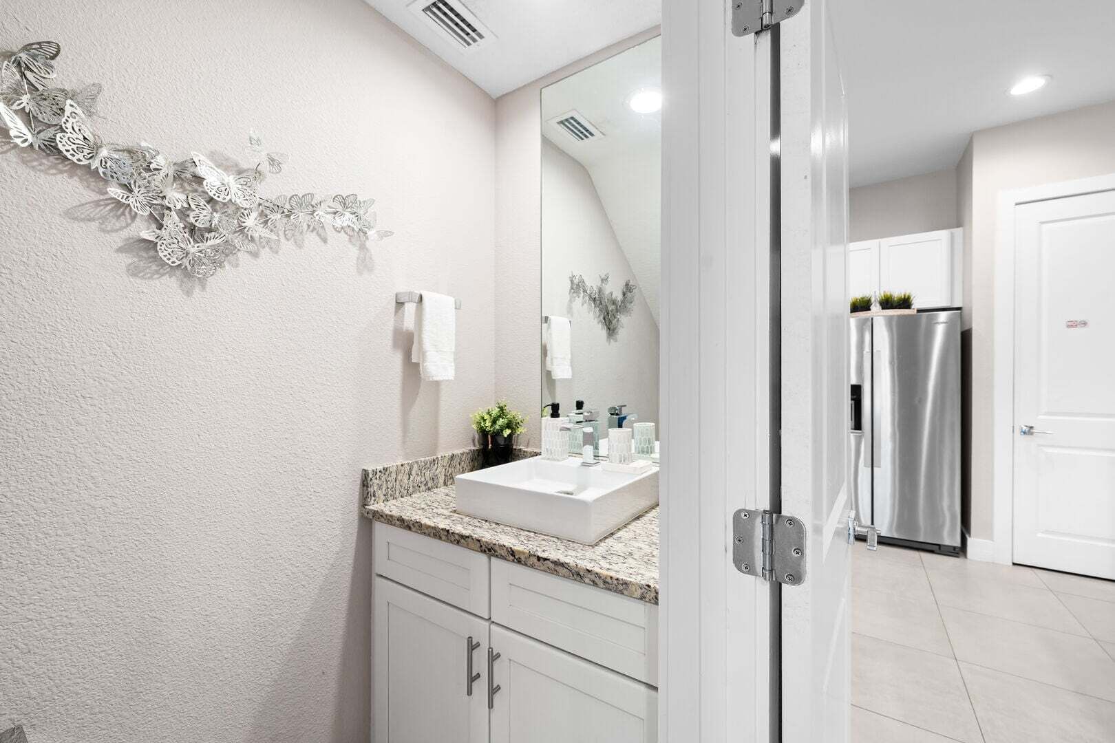 A modern bathroom with a granite countertop, white cabinets, a large mirror, and a decorative wall piece.