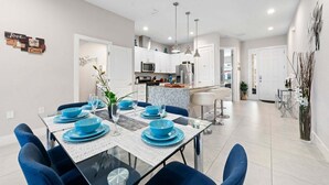 Un comedor moderno con una mesa de vidrio, sillas azules y una cocina al fondo.