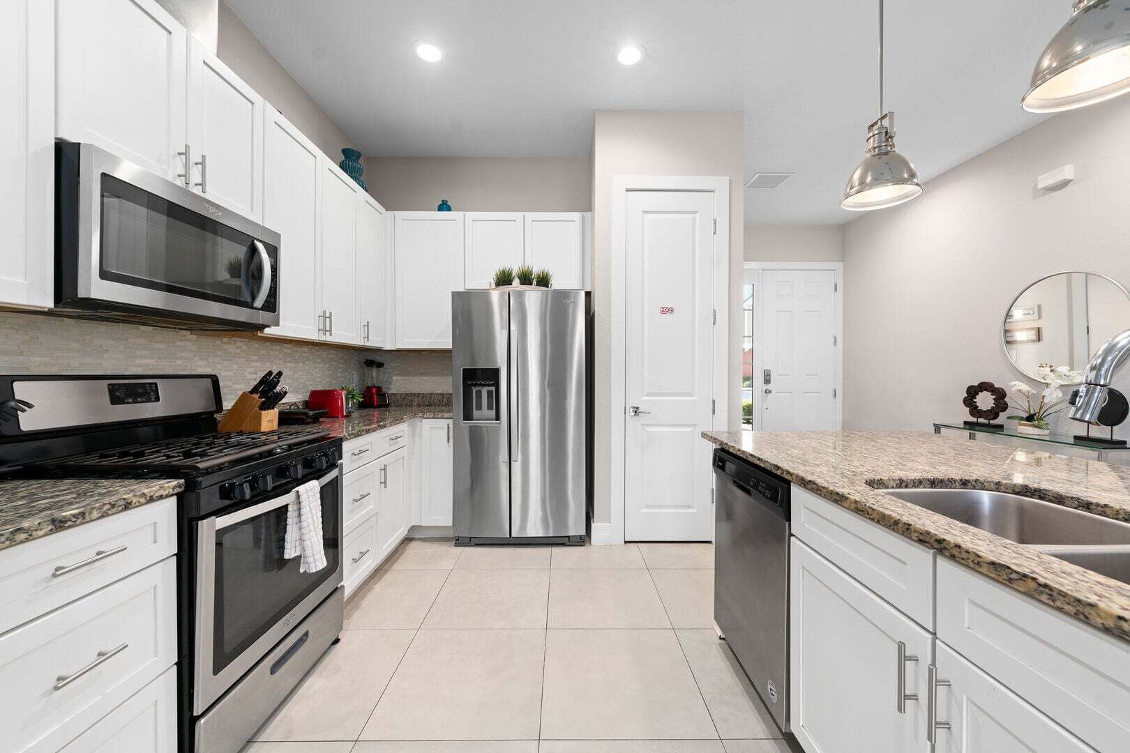 A modern kitchen with white cabinets, stainless steel appliances, granite countertops, and a built-in dishwasher.