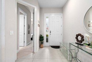 Un couloir avec une porte blanche, une vitrine et une plante en pot.