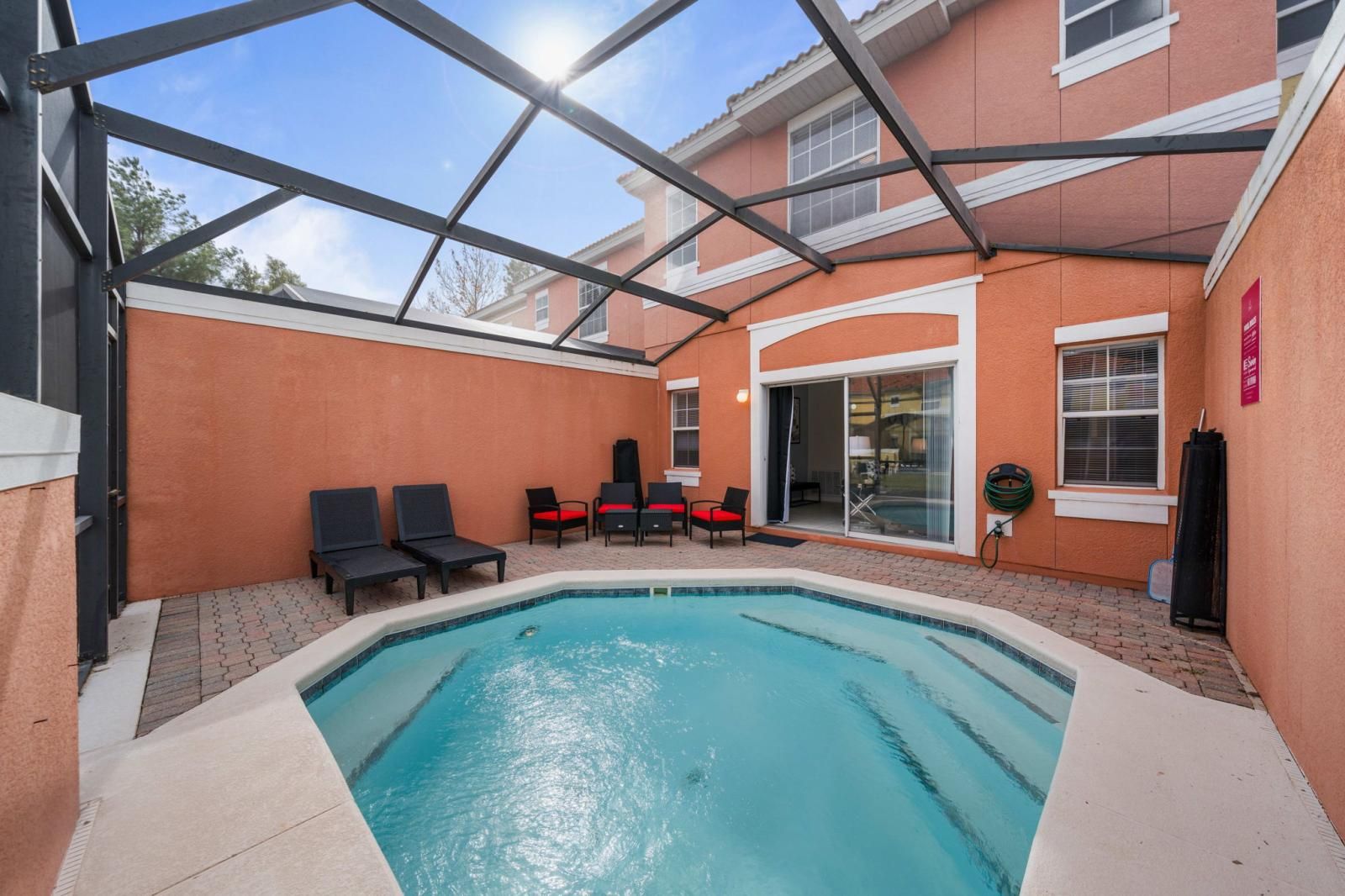 A swimming pool with lounge chairs, a covered patio, and a building with a red exterior.