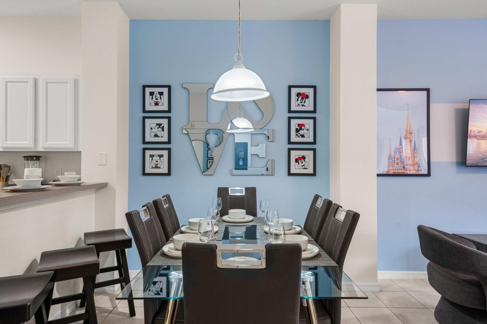 A dining area with a glass table, dark chairs, and a white pendant light.