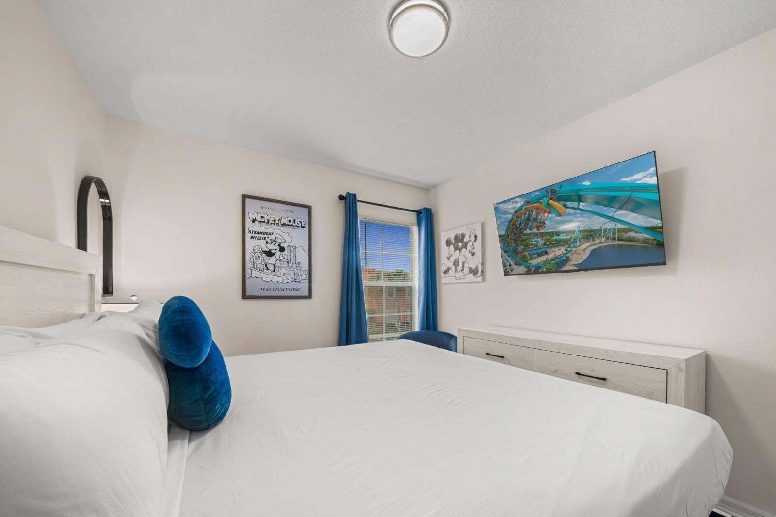 Un dormitorio con cama, ventana con cortinas, un cuadro colgado en la pared y una lámpara en el techo.
