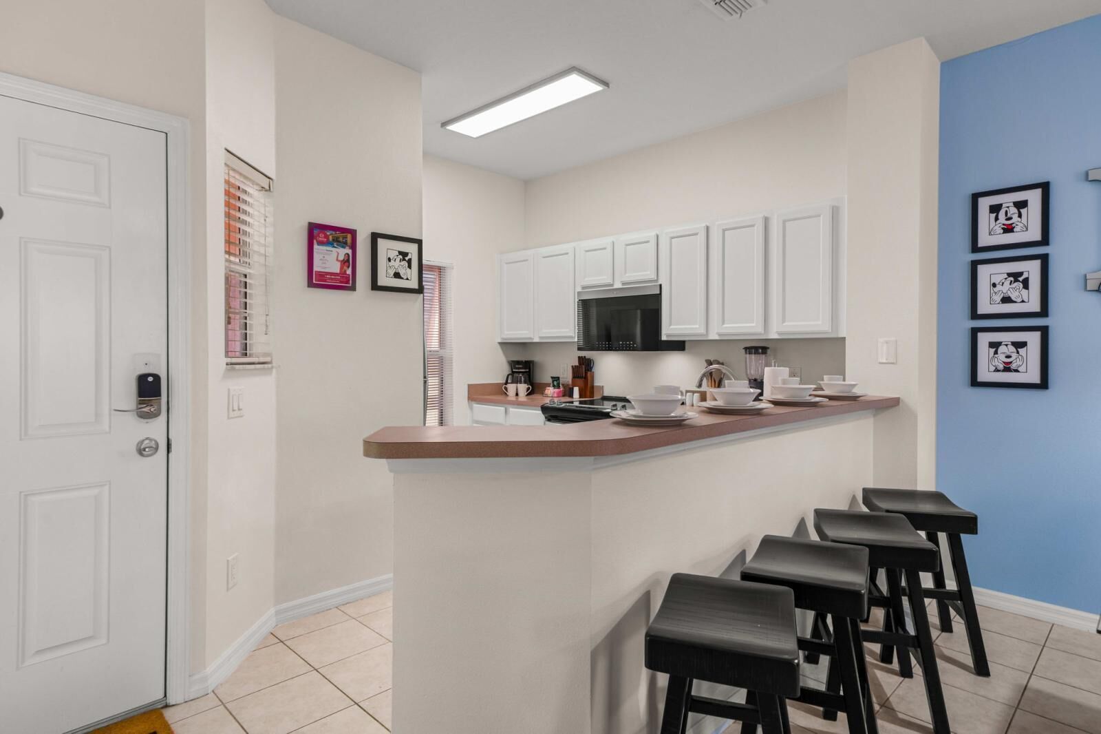 A kitchen with white cabinets, a black microwave, and a bar area with stools.