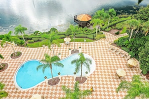 Ein Swimmingpool mit Palmen, einer Laube und einer Terrasse mit Schachbrettmuster.