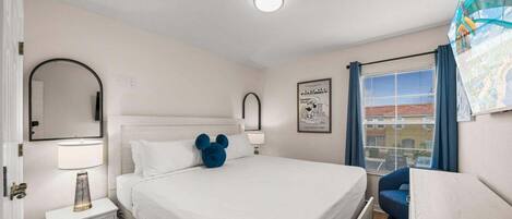 A bedroom with a bed, bedside tables, a mirror, a lamp, a window with curtains, and a wall-mounted picture.