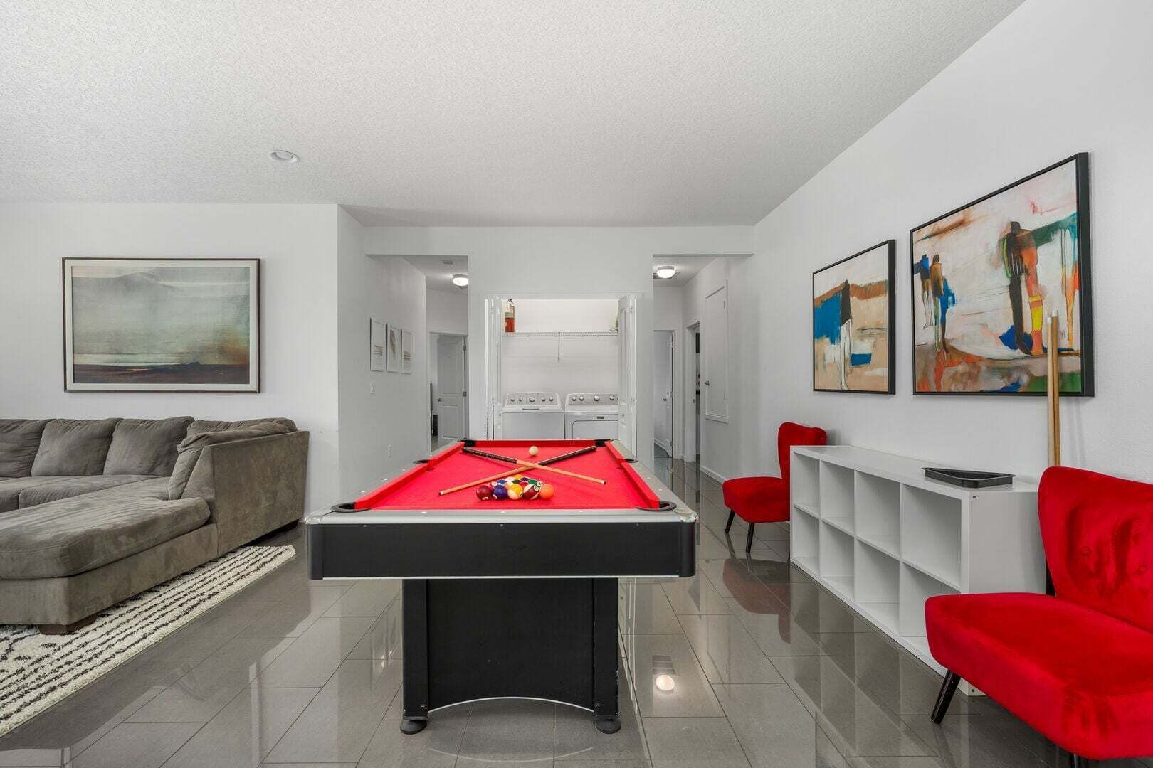 Uma sala de estar moderna com mesa de bilhar, um sofá cinzento e cadeiras vermelhas.