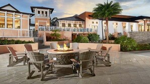 Un patio con mobiliario exterior y una chimenea, rodeado de edificios con balcones y un muro de piedra.