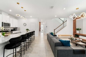 A modern kitchen with a central island, bar stools, and a dining area with a sofa and coffee table. - Theme Dream Lux Vacation Home! (Kissimmee)