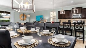 Un comedor con una mesa dispuesta para seis personas, una cocina con armarios oscuros y electrodomésticos de acero inoxidable, y un amplio ventanal con vistas a un jardín.