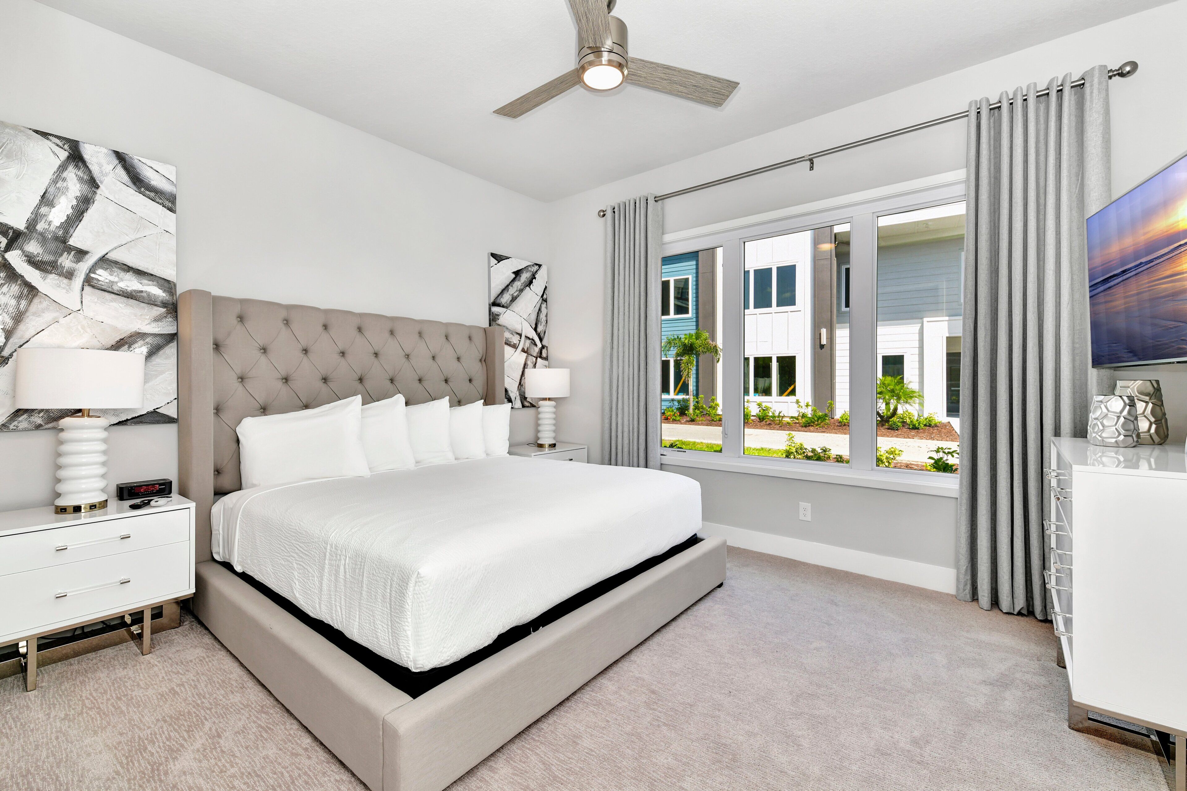 A bedroom with a bed, nightstands, a ceiling fan, a window with curtains, and a view of the outside.