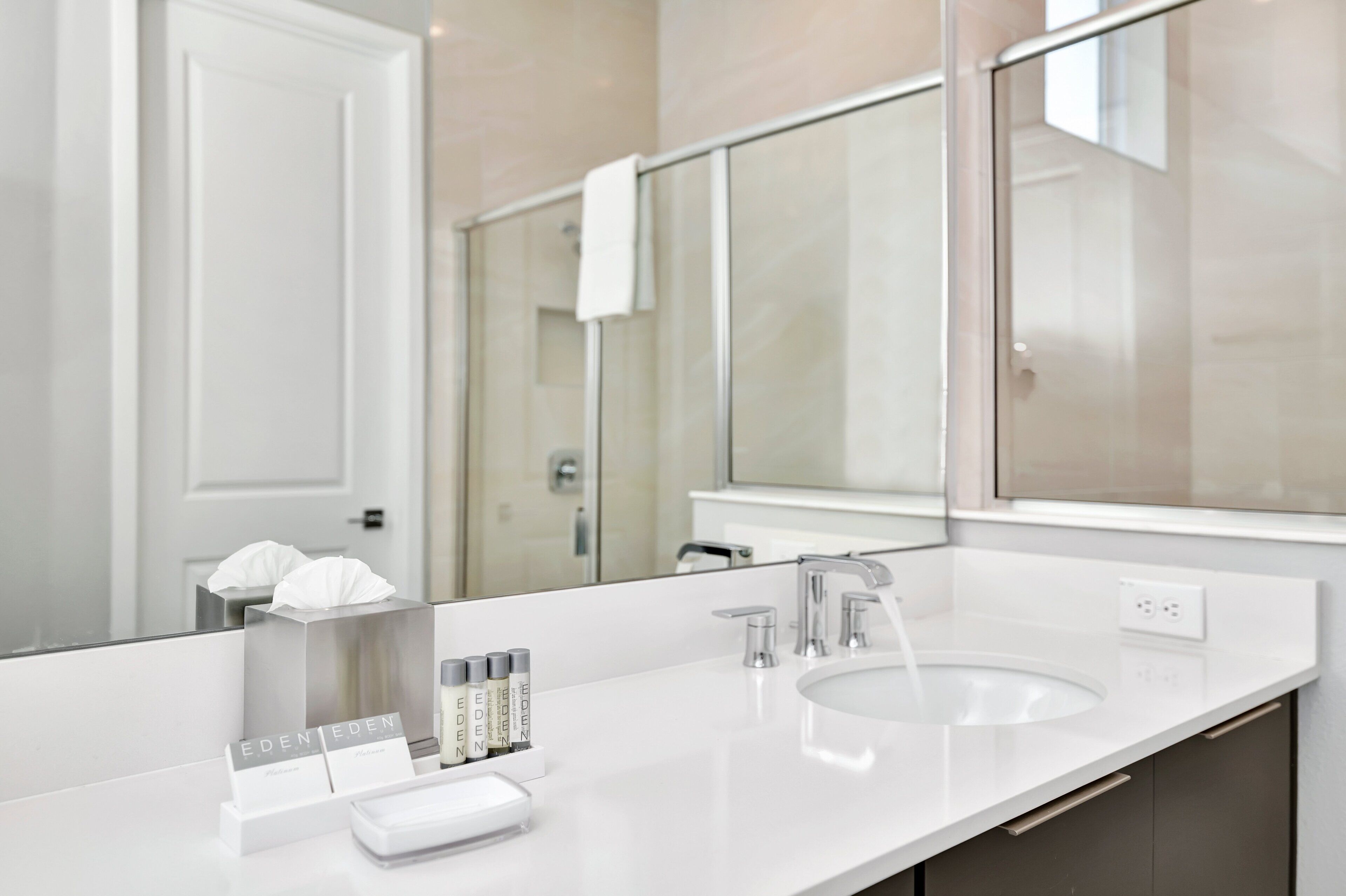 A modern bathroom with a large mirror, a white sink, and toiletries.