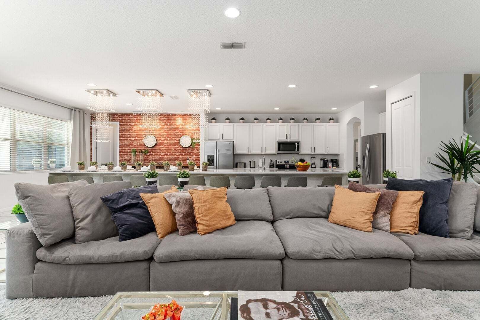 A modern living room with a grey sectional sofa, a glass coffee table, and a kitchen in the background.