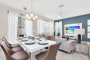 A modern dining area with a white table set for four, a ceiling fan, and a television in the background. - Townhouse w/ Hot Tub Near Disney Sleeps 12 (Kissimmee)