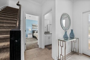 Una escalera con barandilla de madera, un pasillo con un espejo y jarrones, y un dormitorio con pared azul y una cama.