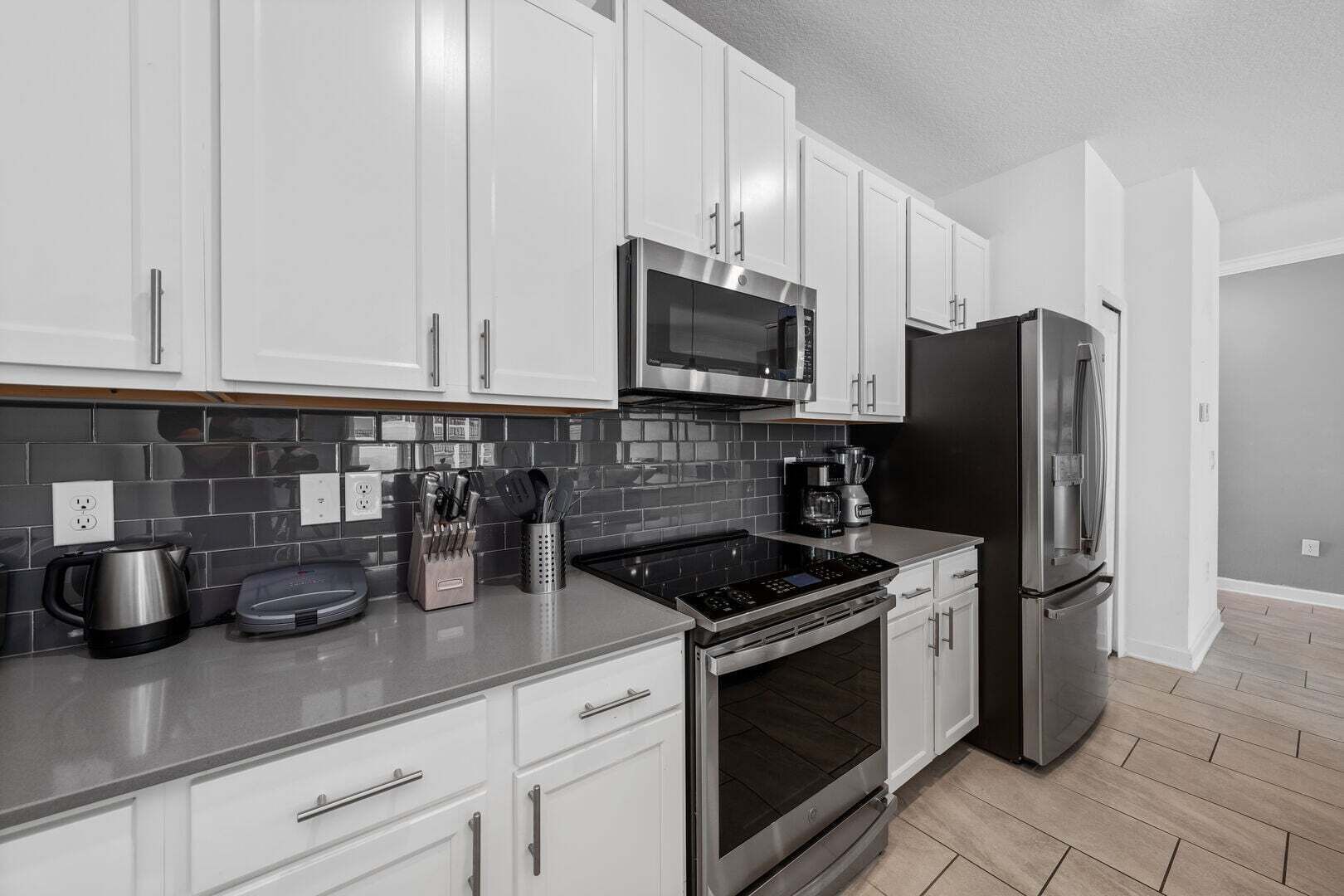 A modern kitchen with white cabinets, a stainless steel microwave, a black refrigerator, and a coffee maker.