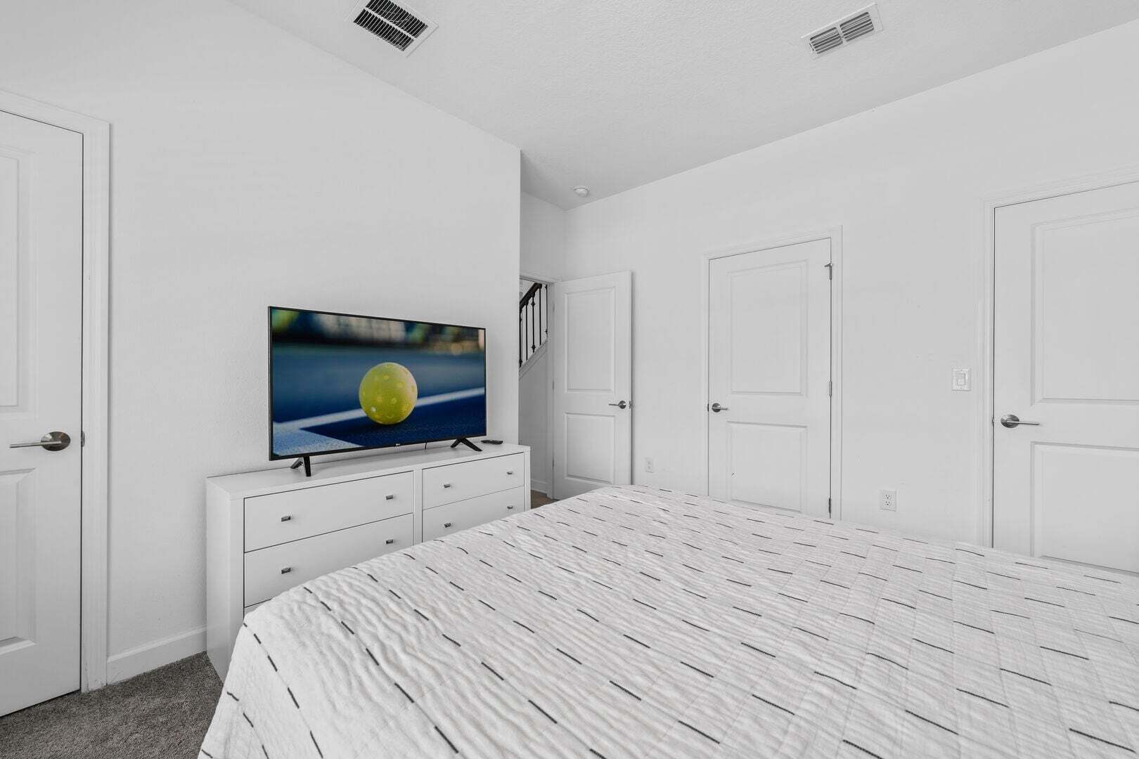A bedroom with a bed, a TV on a dresser, white walls, and doors.