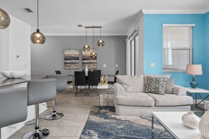 Uma sala de estar moderna com um sofá cinza, uma mesa de centro e um espaço de jantar com mesa e cadeiras.