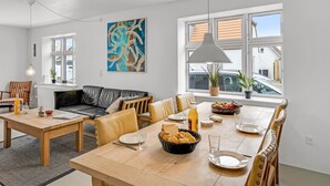 Moderni olohuone, jossa on sohva, ruokapöytä, tuoleja ja suuri ikkuna, josta on kaunis näköala.