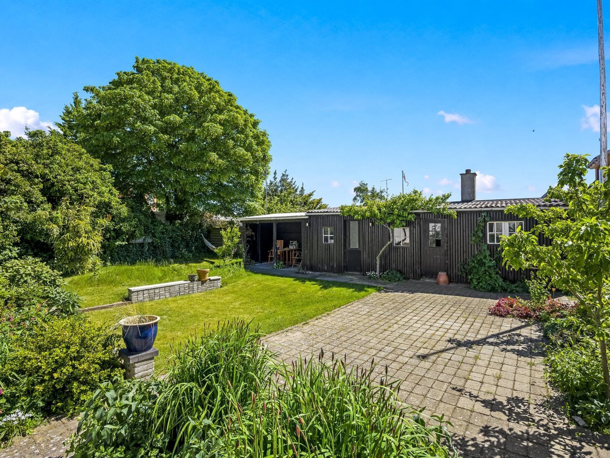 A house with a covered outdoor area, a paved driveway, and a well-maintained garden.