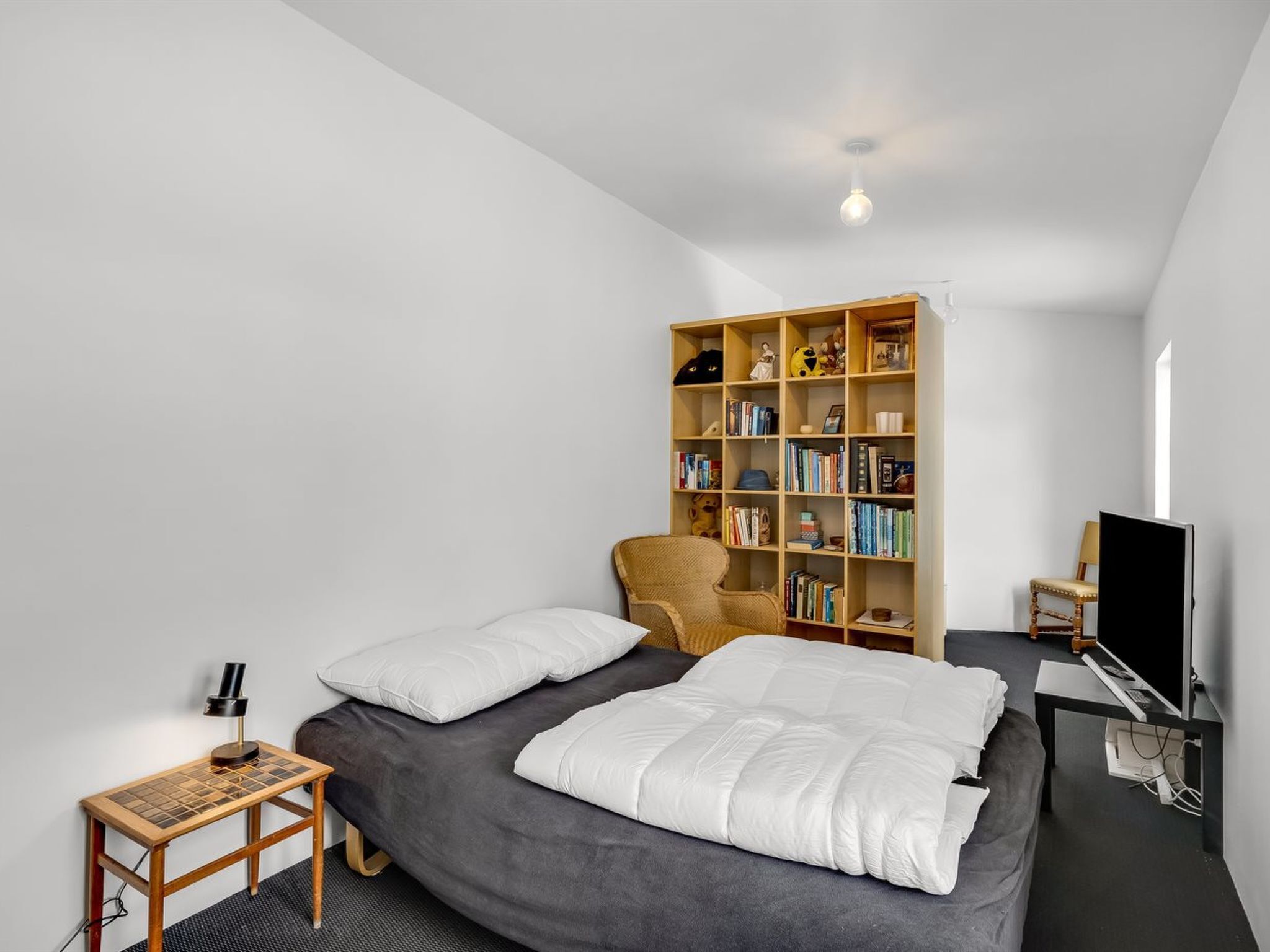A bedroom with a bed, a bookshelf, a chair, a desk, and a television.