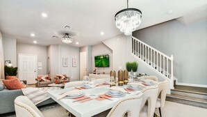 A dining area with a white table set for six, a chandelier, and a staircase leading to another level. - Wonderful House 5 En-suites Free Access to Amazing Resort! (Davenport)