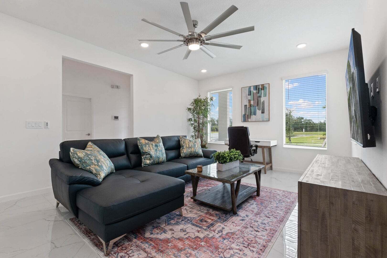 A modern living room with a sectional sofa, a coffee table, a desk, and a ceiling fan.