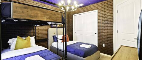 A room with a bunk bed, a single bed, a door, and a starry ceiling.